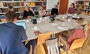 Zu sehen sind die Mitglieder des Instituts für Praktische Theologie. Sie sitzen an einem großen Tisch und unterhalten sich.