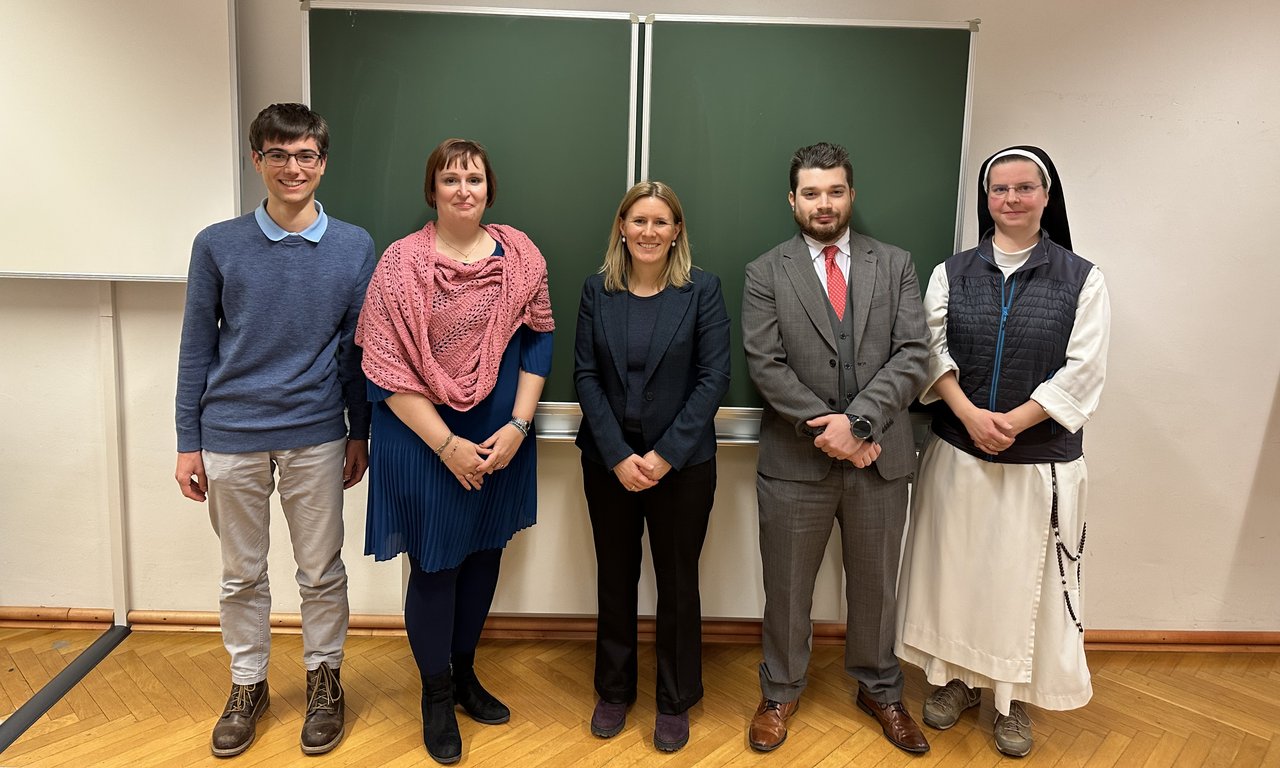 Zu sehen sind Kanzlerin Magdalena Bernhard und Sabine Konrad mit Studierenden. Sie stehen vor einer Tafel.