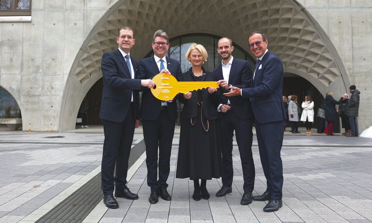 Fünf Personen mit einem großen orangen Schlüssel vor einem Gebäude