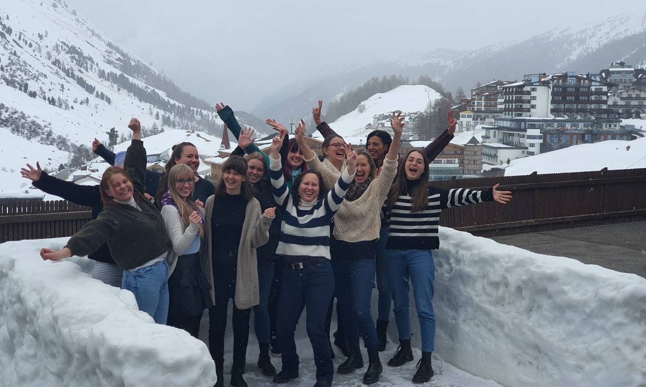 Gruppenfoto im Freien auf einer Terrasse, Schnee im Hintergrund und neben den Personen, die alle sichtbar jubeln.