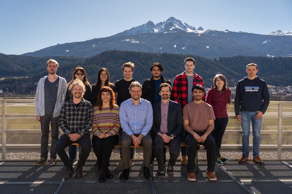 Group picture on a roof with mountains and a cloudy sky in the background.
