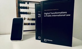 Das Buch „Global Transformations in Public International Law“ vor einem Rechenschieber und einem Handy.