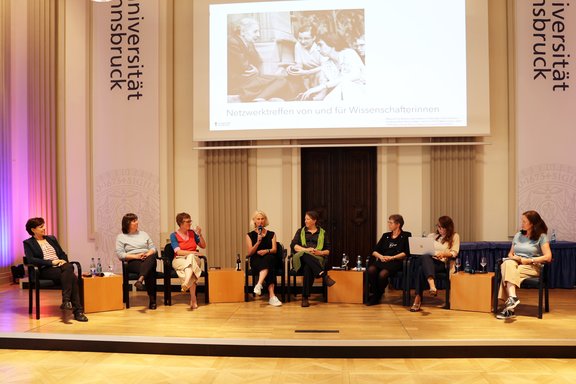 Am Podium in der Aula sitzen acht Frauen, im Hintergrund eine Leinwand.