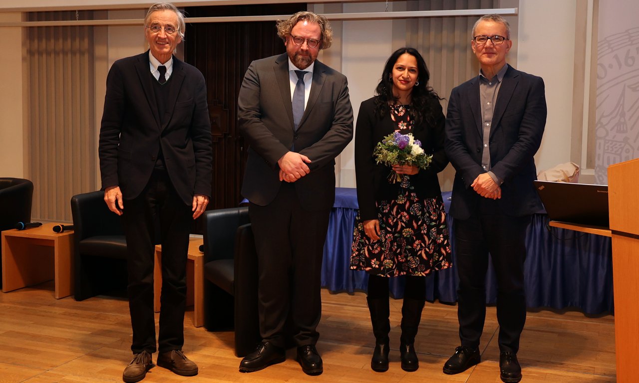 Drei Männer und eine Frau stehen für ein Gruppenfoto nebeneinander, die Frau hat einen Blumenstrauß in der Hand.