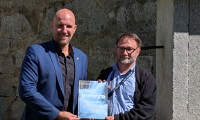 Die beiden Herausgeber schauen in die Kamera und halten zu zweit den Tagungsband in den Händen.