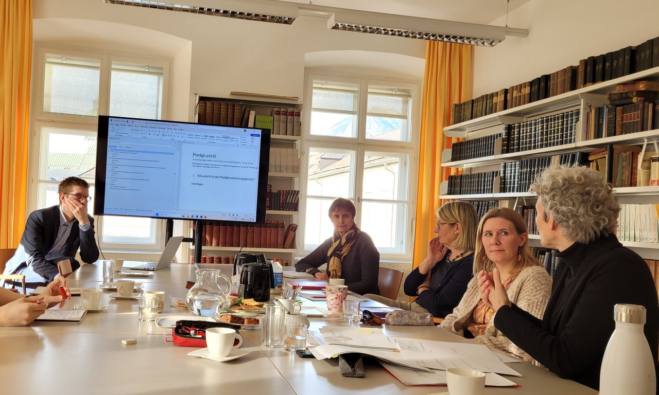 Zu sehen sind Mitglieder des Instituts für Praktische Theologie. Sie sitzen an einem großen Tisch, sie arbeiten gemeinsam und diskutieren.