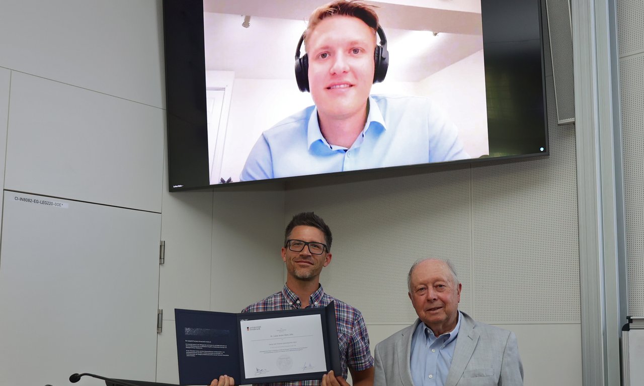Gruppenfoto mit drei Personen, wobei eine Person auf einem Bildschirm zugeschalten ist.