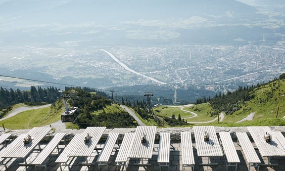 View of Innsbruck from the top of a nearby mountain. In the foreground there is a cable car and some tables.