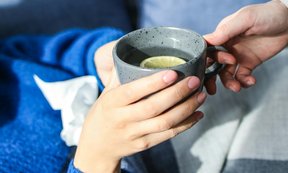 Person reicht einer erkälteten Person eine Tasse Tee