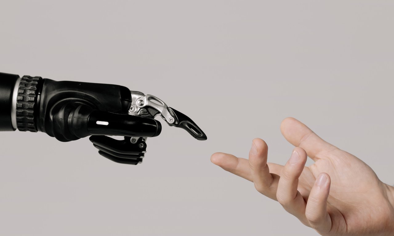 Symbolbild: Roboterhand und Menschenhand berühren einander fast mit ausgestreckten Zeigenfingern.