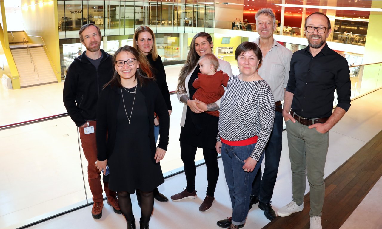 Seven people stand in front of a brightly lit room