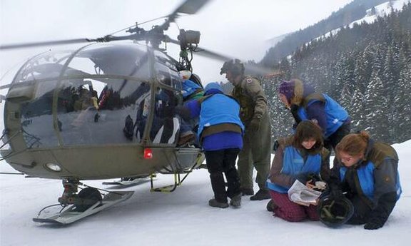 Six people in front of a helicopter in the snow