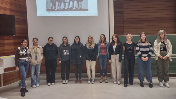 Group photo of workshop participants in a lecture hall. They stand in a line net to each other, sorted by size (smallest on the left, tallest on the right).