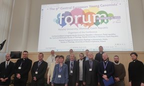 Zu sehen sind die Teilnehmer und Teilnehmerinnen des „9th Central European Young Canonists forum”. Sie stehen. Im Hintergrund sieht man eine Bildschirmpräsentation.