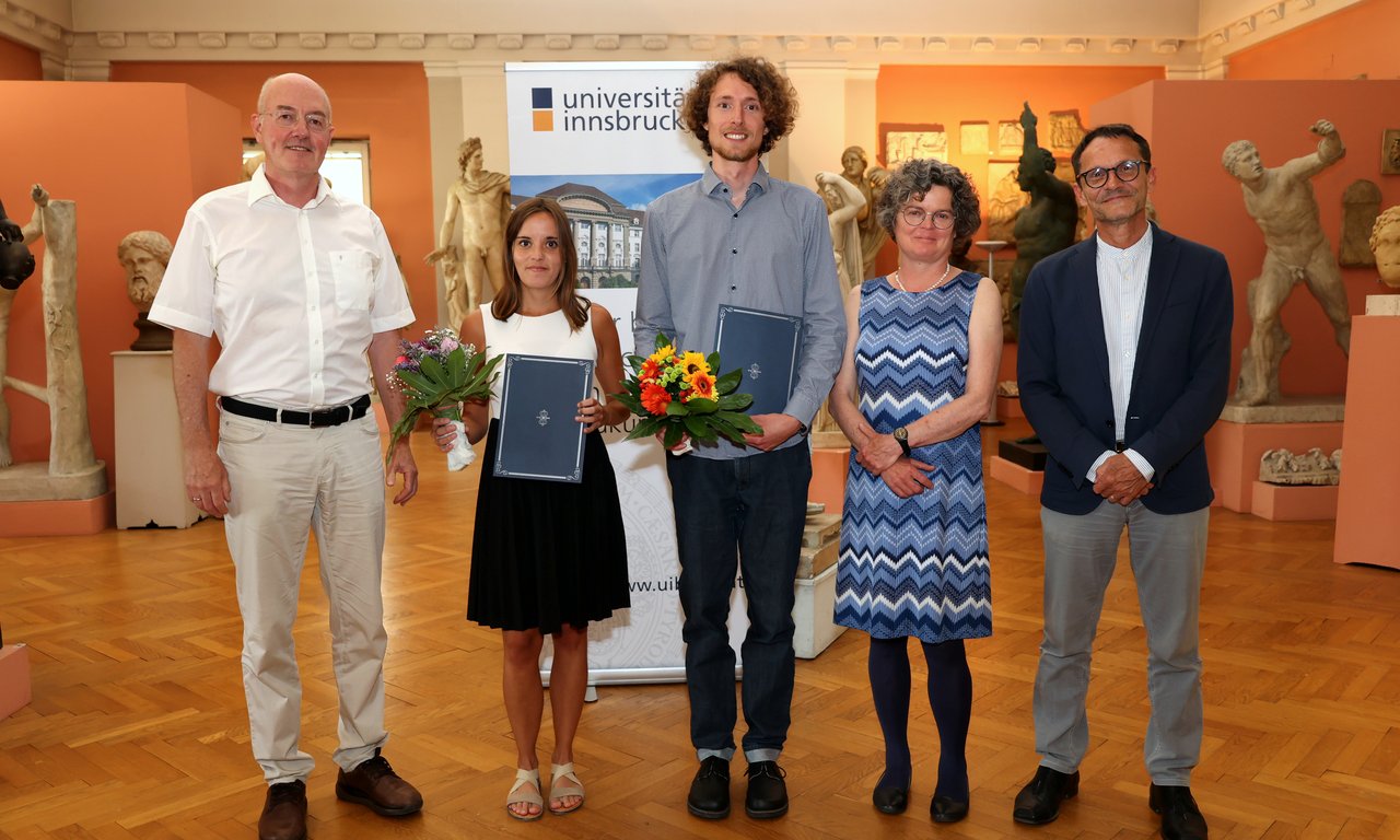 Fünf Personen stehen in einer Reihe und blicken in die Kamera, im Hintergrund antike Statuen
