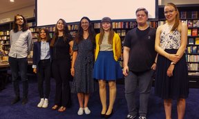 Sieben Personen posieren in einer Buchhandlung für ein Gruppenfoto