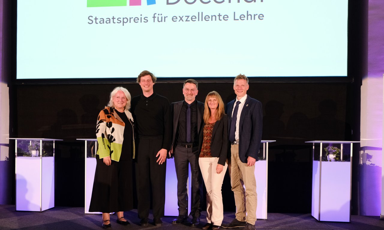 Fünf Personen stehen auf einer Bühne, dahinter eine Leinwand mit dem Schriftzug "Ars Docendi"