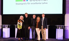 Fünf Personen stehen auf einer Bühne, dahinter eine Leinwand mit dem Schriftzug "Ars Docendi"