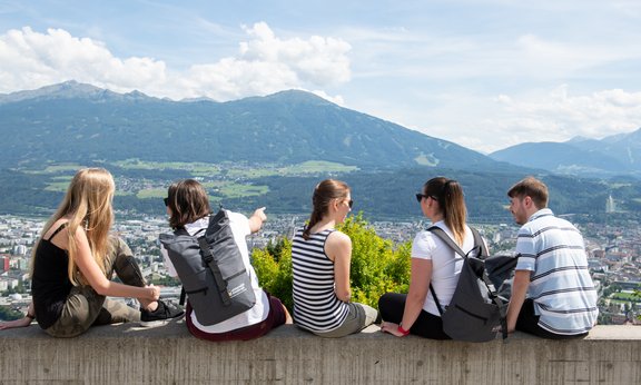 Studierende sitzen auf einer Mauer und überblicken die Landschaft
