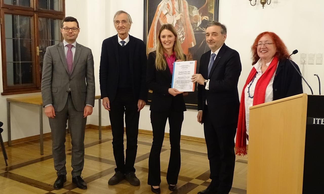 Fünf Personen stehen für ein Gruppenfoto nebeneinander, eine Frau hält eine Urkunde.