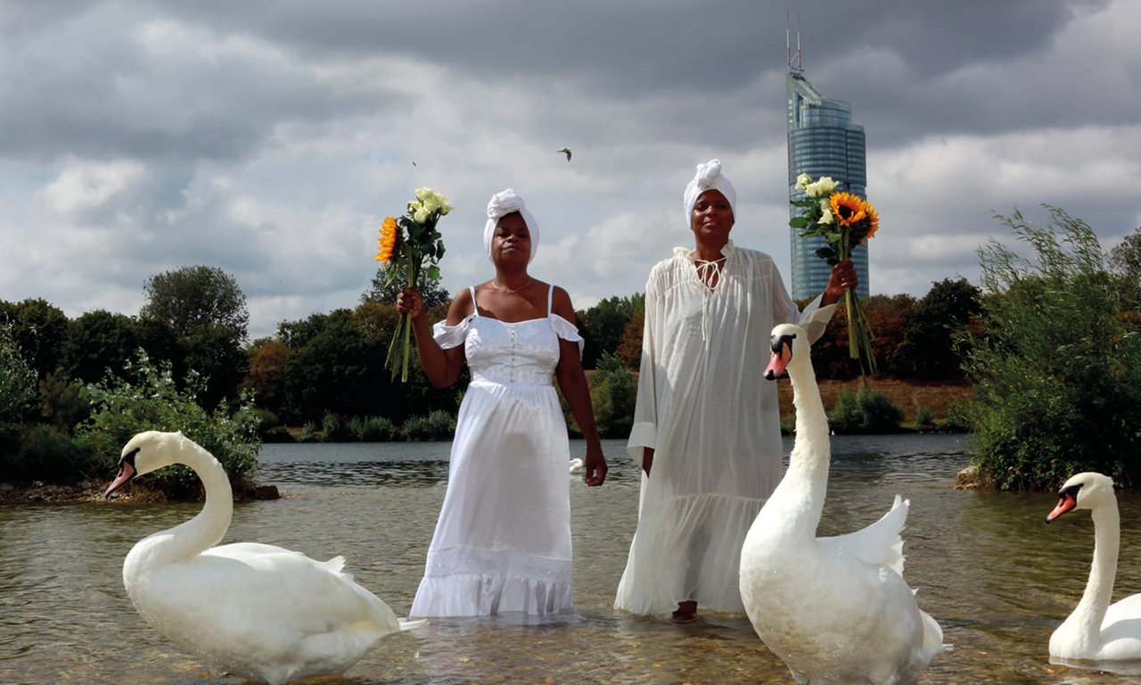 Zwei Personen stehen im Wasser, um sie herum schwimmen Schwäne.