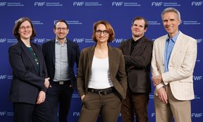 Fünf Personen stehen in einer Reihe und blicken in die Kamera, im Hintergrund eine blaue Leinwand.