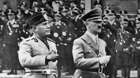 Mussolini und Hitler marschieren nebeneinander vor einer Menge an Soldaten