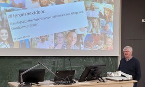 Zu sehen ist Professor Hans Mendl. Er steht vor einer Tafel in einem Hörsaal. Eine Bildschirmpräsenation ist zu sehen.