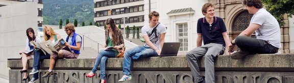 Studierende sitzen auf einer Mauer mit der Aufschrift "Universität Innsbruck" vor der Geiwi
