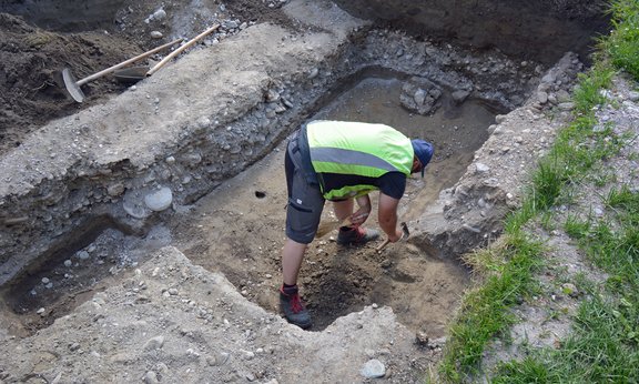 Eine Person mit einer gelben Schutzweste steht in einer Mulde und bückt sich