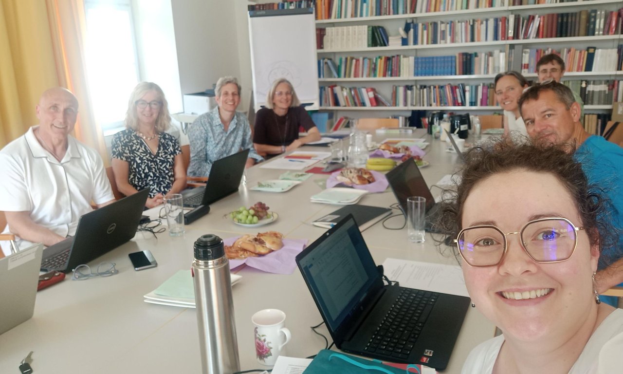 Zu sehen sind das Team des Bischöflichen Schulamtes sowie die Mitglieder des Fachbereiches Religionspädagogik. Die Personen sitzen an einem großes Tisch. Sie haben Laptops, Schreibutensilien, Getränke und Snacks vor sich.