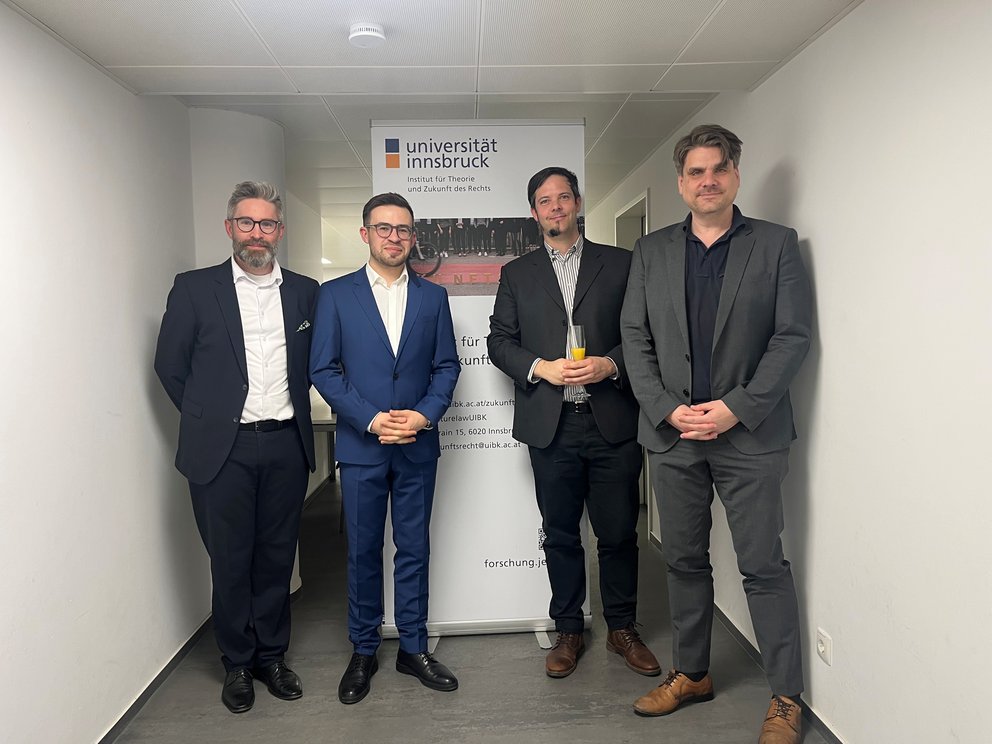 Vier Männer vor einem Roll-up des Instituts für Theorie und Zukunft des Rechts