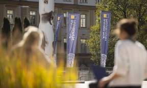Banner der Universität Innsbruck, im Vordergrund zwei Personen von hinten