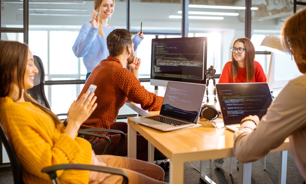 5 Studierende im Austausch bei der Arbeit mit Computern, die am Bildschirm mit Programmiersprache zu sehen ist.