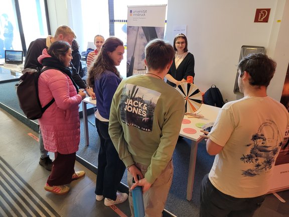 Zu sehen sind junge Erwachsene. Sie stehen vor dem Informationsstand der Katholisch-Theologischen Fakultät.