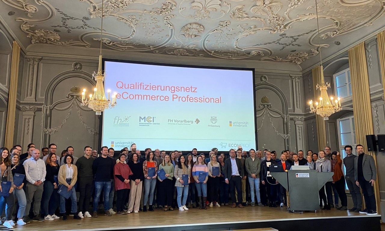 Bühne in einem großen Hörsaal, es stehen rund 60 Personen mit Urkunden für ein Gruppenbild zusammen.