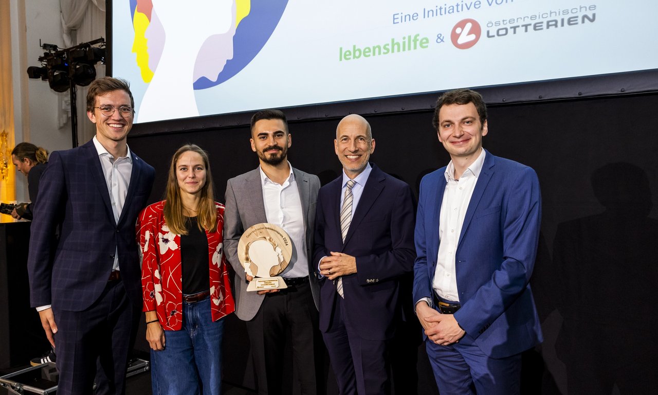 Gruppenfoto mit fünf Personen, im Hintergrund eine Leinwand, von der nur der untere Bereich zu sehen ist.