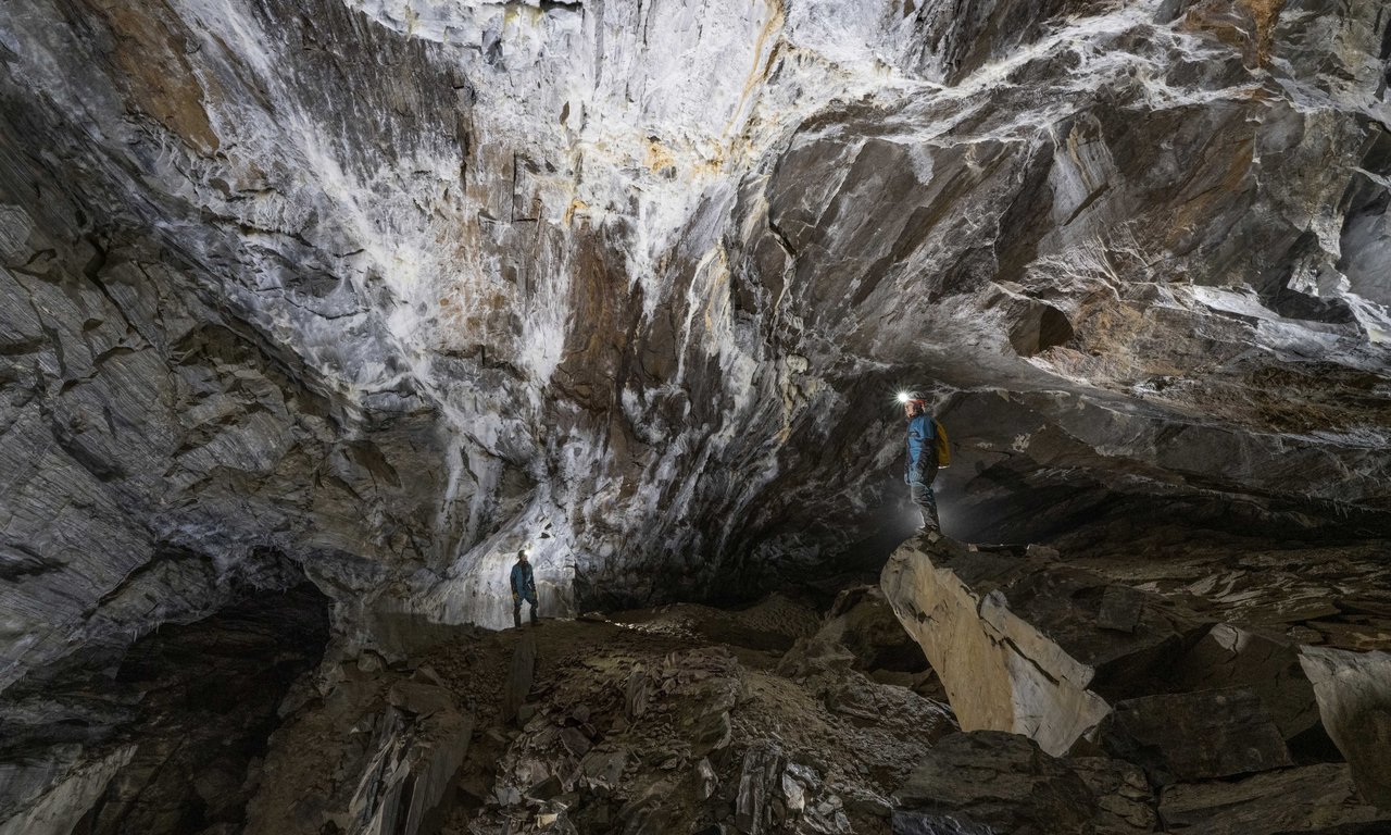 Blick in ein Höhle, ein Forscher leuchtet den großen Höhlenraum mit einer Stirnlampe aus.