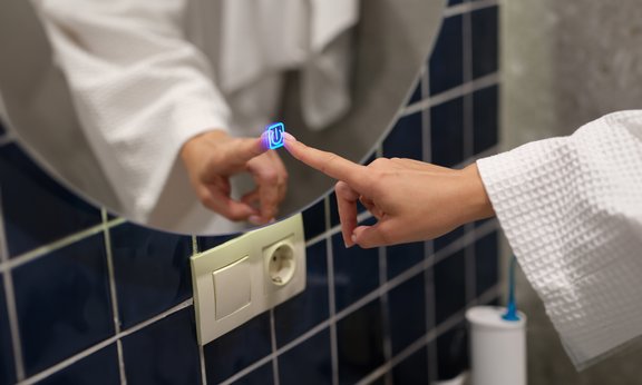 Ein Finger drückt einen blau leuchtenden Schalter in einem Spiegel