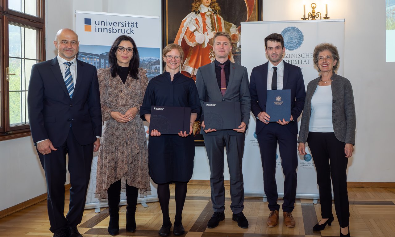 Sechs Personen stehen für ein Gruppenfoto nebeneinander, hinter ihnen sind Roll-ups mit den Logos der Universitäten.