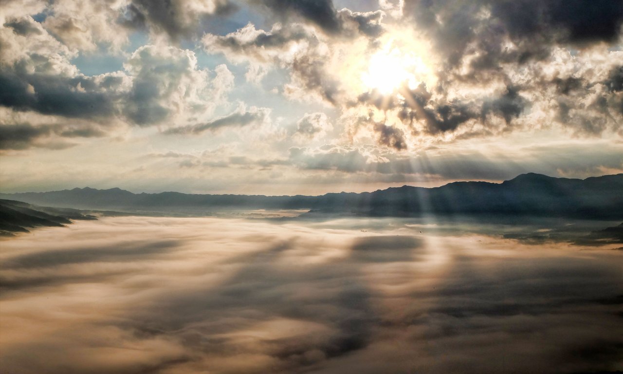 Sonnenstrahlen scheinen durch Wolken, im Hintergrund Berge