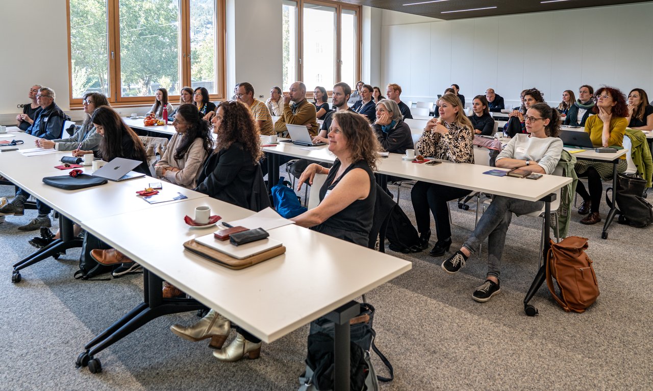 Blick von rechts vorne in einen großen Seminarraum, die Reihen sind komplett besetzt.
