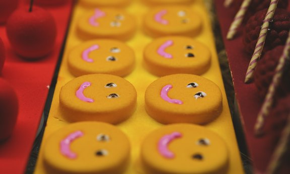 Zehn gleiche Kekse mit aufgemaltem Gesicht aus Zuckerguss liegen in Zweierreihe auf einer länglichen Platte