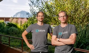 man sieht die beiden Geschäftsführer von Txture und im Hintergrund einen Baum, blauer Himmel und hinten einen Berggipfel