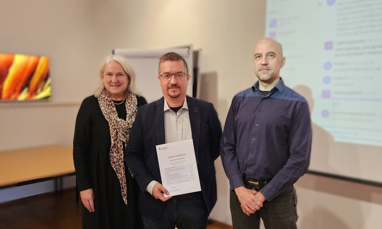 Auf dem Bild zu sehen sind drei Personen. Janette Walde, Thomas Monz und Tim Netzer. Thomas Monz erhält sein Zertifikat Lehrkompetenz.