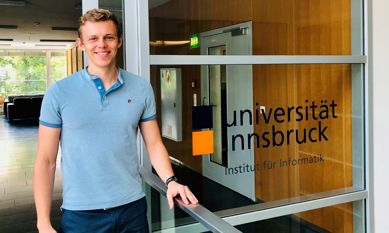 Das Bild zeigt Eduard Frankford im Gang des Instituts für Informatik im ICT Gebäude neben dem Universitätslogo.