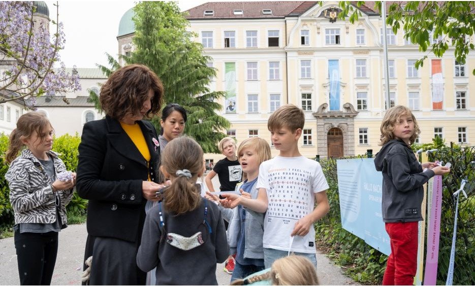 Kinder und Lehrer der VS montieren mit der Kuratorin Spruchbänder am Zaun der VS (Credit: Wolfgang Lackner)