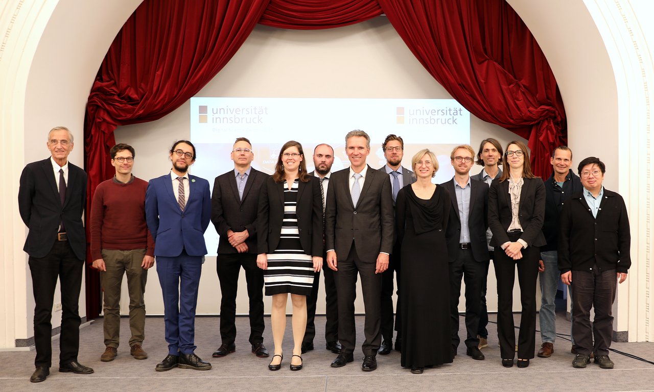 14 Personen stehen für ein Gruppenfoto auf einer Bühne