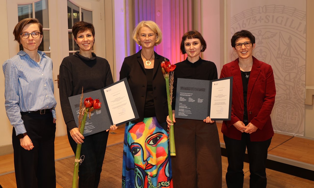 Zu sehen sind die Preisträger:innen mit Blumen und Urkunde gemeinsam mit den Betreuer:innen und der Rektorin der Universität