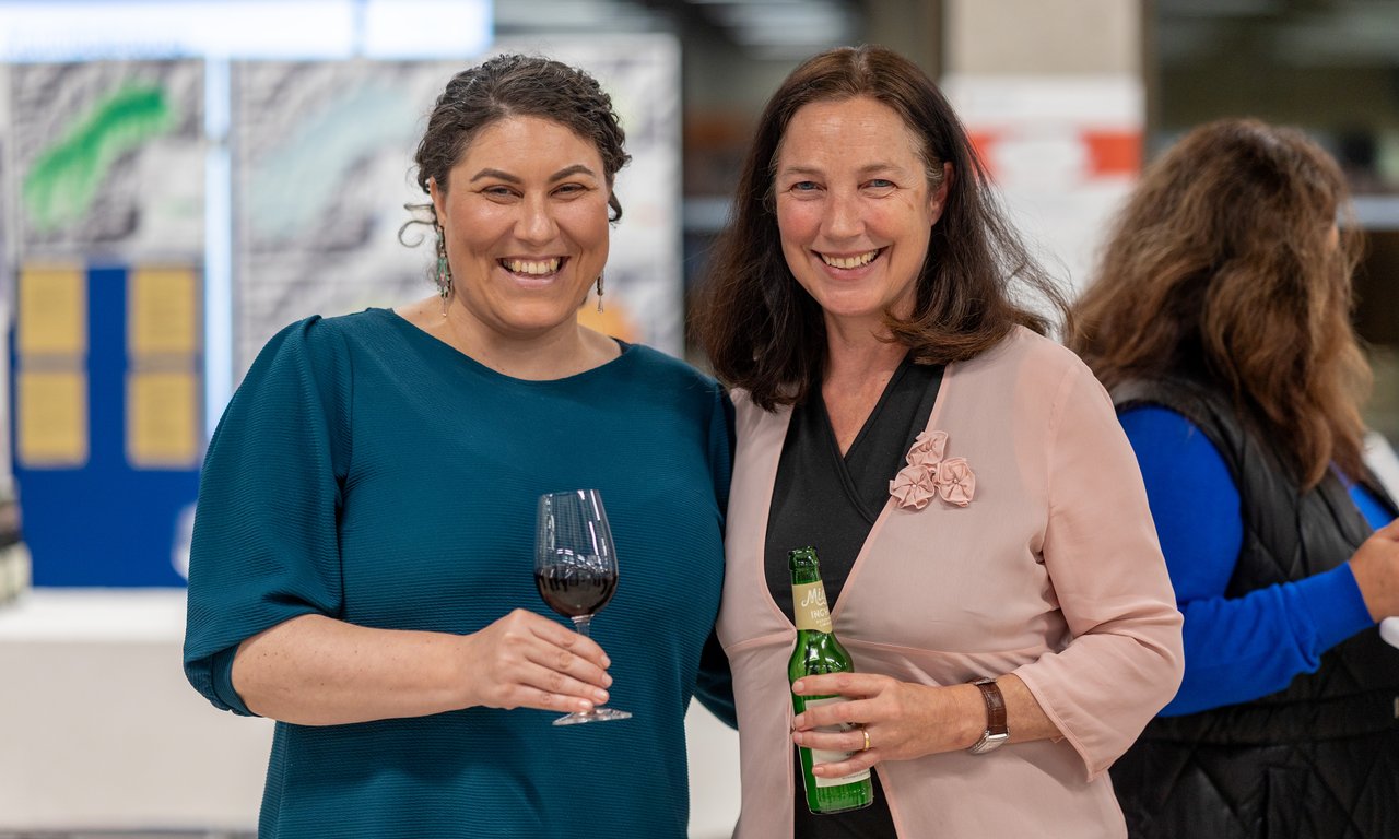 Zwei lächelnde Frauen stehen nebeneinander und halten ein Glas Sekt in der Hand.